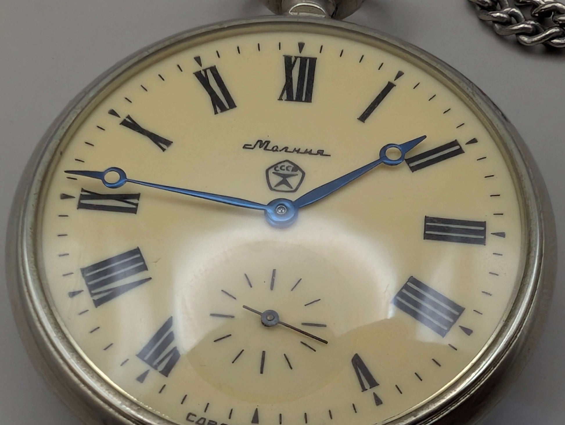 Close-up of vintage Molnija pocket watch face with Roman numerals and blue hands, featuring Soviet Union emblem from 1980s.